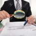 54598245-photo-of-businessman-analyzing-bills-with-magnifying-glass